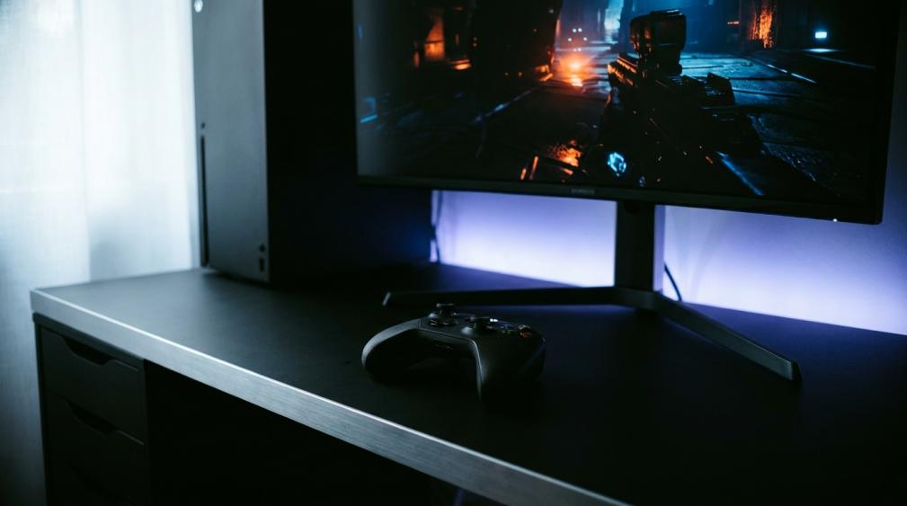 Gaming monitor displaying HDR content with a console controller on desk in a dark room