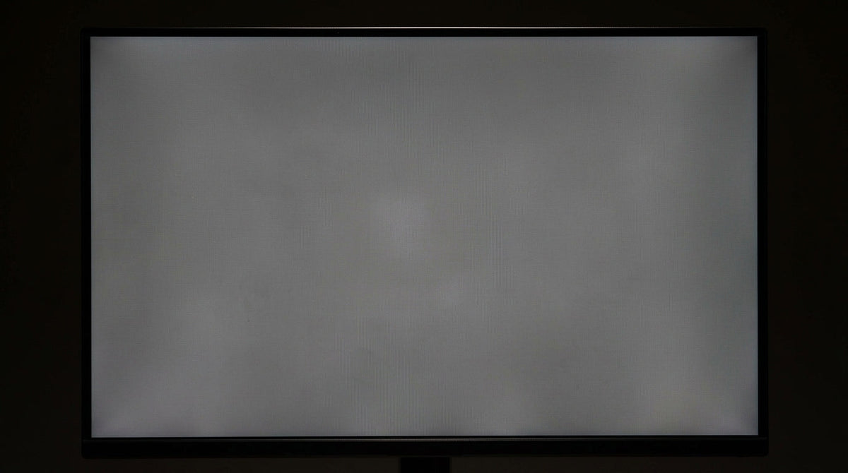 A close-up shot of a computer monitor displaying a solid gray background with visible cloudy splotches and uneven patches, illustrating the dirty screen effect.