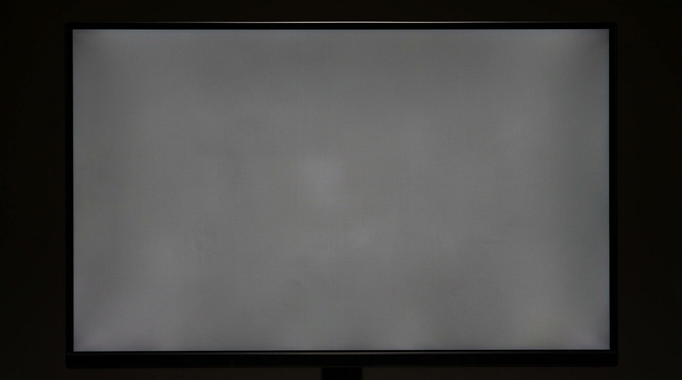A close-up shot of a computer monitor displaying a solid gray background with visible cloudy splotches and uneven patches, illustrating the dirty screen effect.